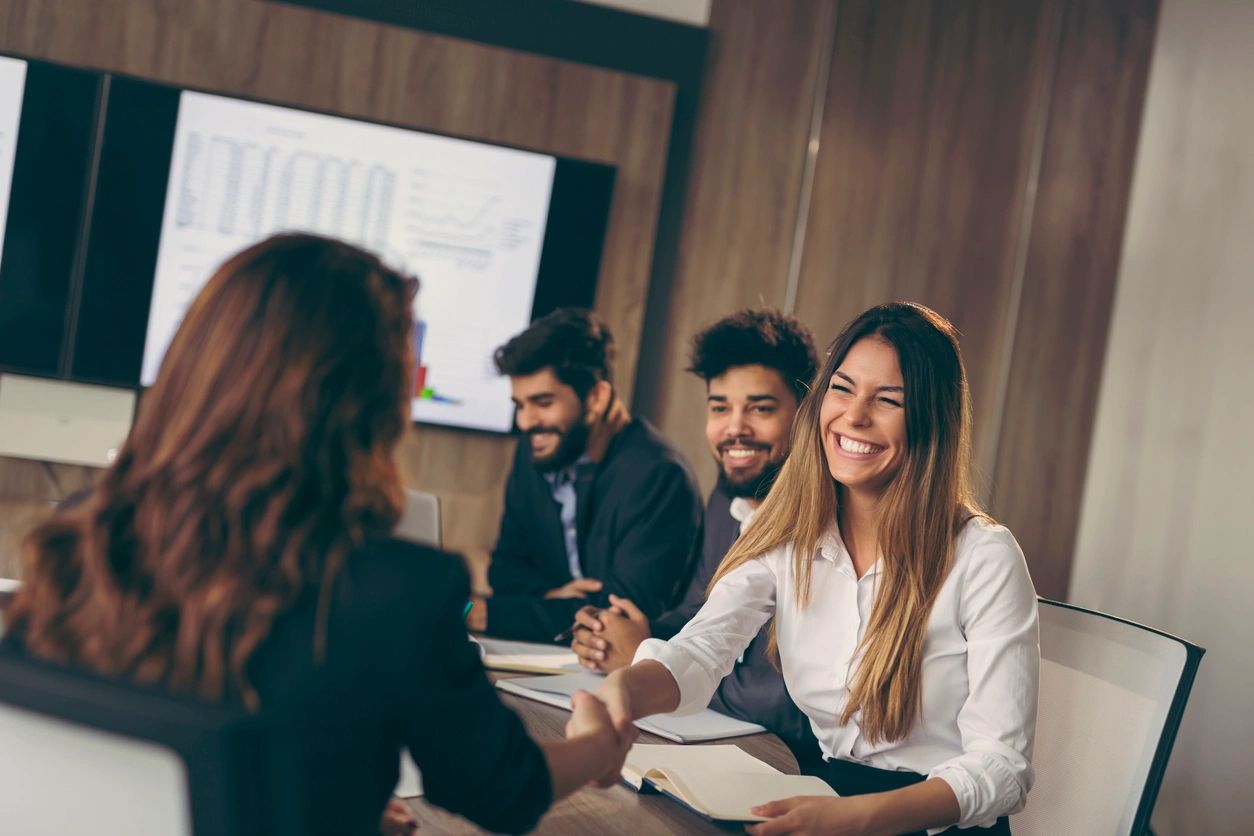 Two smiling accountants sitting at a conference room table with a male client. The accountants are reviewing financial paperwork and forms with the client.